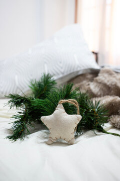 A charming, rustic Christmas scene featuring a handmade fabric star ornament nestled against a pine branch on white bedding. The soft focus and natural light create a warm, festive holiday mood.