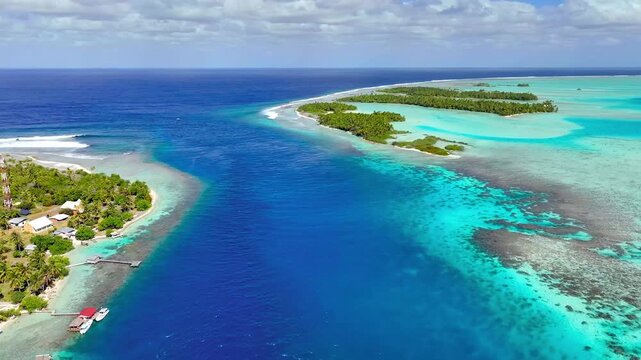 Aerial view of tropical island pass between coral reefs under sunny sky in French Polynesia paradise.