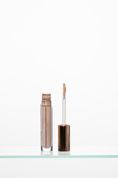 Luxury liquid concealer tube in a neutral beige shade, featuring a doe-foot applicator ready for use. essential makeup base product concept