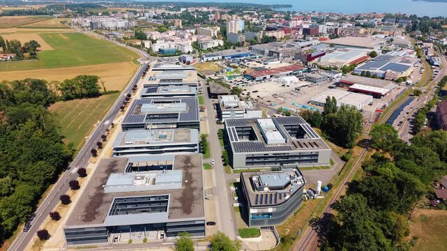 Aerial view of the modern office buildings and industrial facilities at Rte de Crassier 11, surrounded by green fields and infrastructure in Eysins, Vaud, Switzerland.
