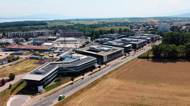 Aerial view of modern office buildings at Rte de Crassier 11, surrounded by fields and roads in Eysins, Vaud, Switzerland.