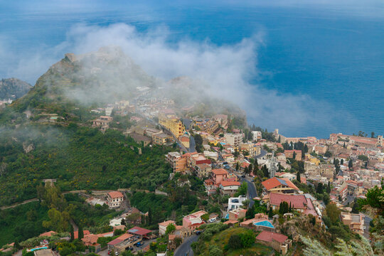 Scenic island town nestled on a green hill above clouds overlooking the sea