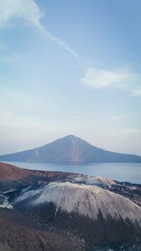 Volcanic Island Landscape with Crater Foreground Over Calm Sea Under Soft Blue Sky. Drone shot of Mount Krakatoa