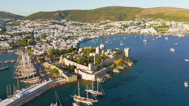 Bodrum, Turkey. Bodrum Castle, massive stone fortress with crenellated walls and towers, aerial drone view over turquoise harbor filled with yachts under clear summer sky. Aerial View