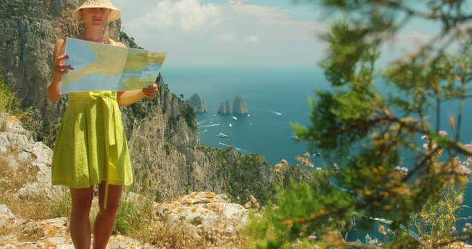 Woman reading a map on cliff with sea view and distant Faraglioni stacks on Capri island