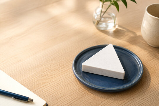 White equilateral triangle paperweight on blue ceramic coaster, neutral still life for editorial header