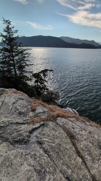 Rocky shores of islands and peninsulas with trees and evergreens in Burrard Inlet on a sunny summer day. Beautiful nature in British Columbia, Canada.