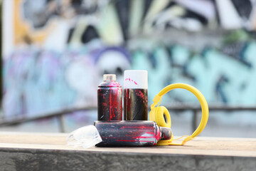 Urban street art and creative expression, spray paint cans and yellow headphones on a wooden bench with graffiti background for youth culture lifestyle © Pixel-Shot