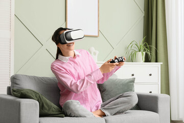 Virtual reality gaming and metaverse entertainment, happy woman playing video games with vr headset and controller on a sofa in a modern living room © Pixel-Shot