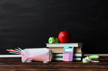 Back to school education concept, stack of books with apple and stationery supplies on wooden desk against black chalkboard background for classroom © Pixel-Shot