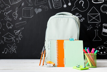 Back to school education concept, student backpack with notebooks and stationery supplies on a classroom chalkboard background with hand drawn doodles © Pixel-Shot