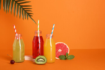 Healthy lifestyle and summer refreshment, assorted fruit juices in glass bottles with straws and fresh tropical fruits on a bright orange background © Pixel-Shot