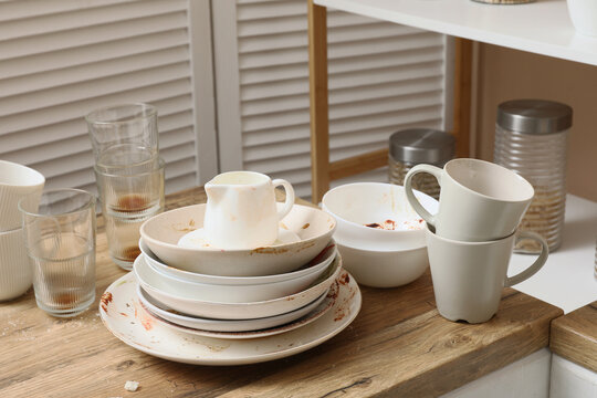 Household chores and domestic mess, stack of dirty dishes and stained plates on a wooden kitchen counter after a meal with cluttered dining area