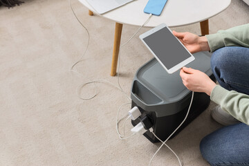 Energy independence and portable power, person charging tablet and mobile devices with a high capacity power station during a home electricity outage © Pixel-Shot