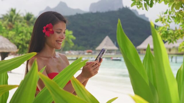 Asian beauty woman using phone in bikini on tropical beach. Beautiful young woman on vacation and travel using smartphone app. Raw unedited video of real woman model without any makeup