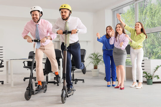 Workplace fun and office culture, business team racing on electric scooters with colleagues cheering in modern corporate office environment