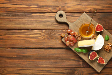 Obraz premium Board with pieces of tasty Camembert cheese, fresh ripe figs and bowl of honey on wooden background