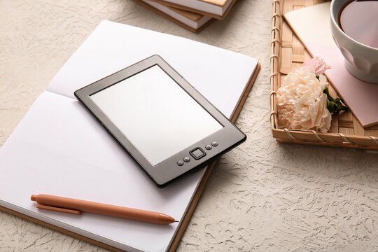 Modern e-reader with notebook, cup of tea and flowers on white background