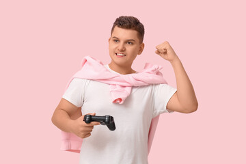 Teenage boy with game pad celebrating success on pink background © Pixel-Shot
