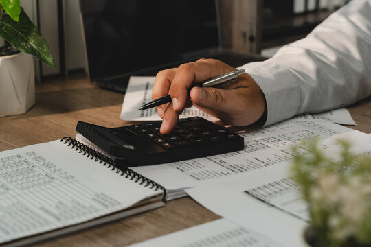 Businessman using calculator with pen over printed budget reports for budget planning, expense management, financial analysis and accounting review.
