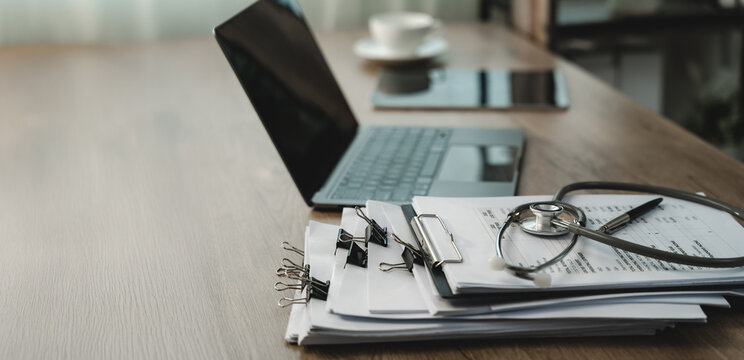 Stethoscope on financial reports beside laptop, showing healthcare finance, medical cost analysis, accounting documents and business reporting with copy space.