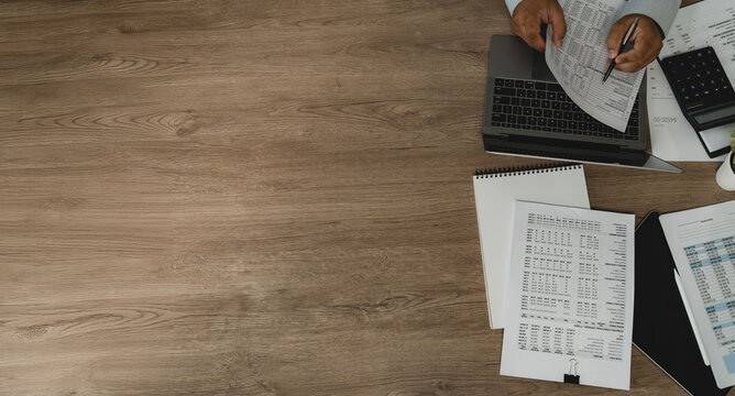 Businessman reviewing budget report beside laptop, calculator and tablet with wide copy space for budget planning, financial planning and financial analysis.
