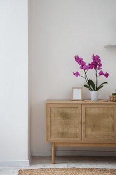 Wooden commode with orchid flower and frame near light wall in room