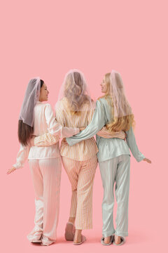Young woman and her bridesmaids in pajamas hugging on pink background, back view. Hen Party