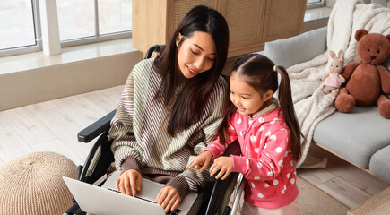 Disability inclusion and remote work, mother in wheelchair using laptop with daughter at home for...