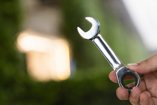 Handyman tool and mechanical repair concept with hand holding shiny steel ratchet wrench against green tree bokeh background for home maintenance, technical service and plumbing fixing.
