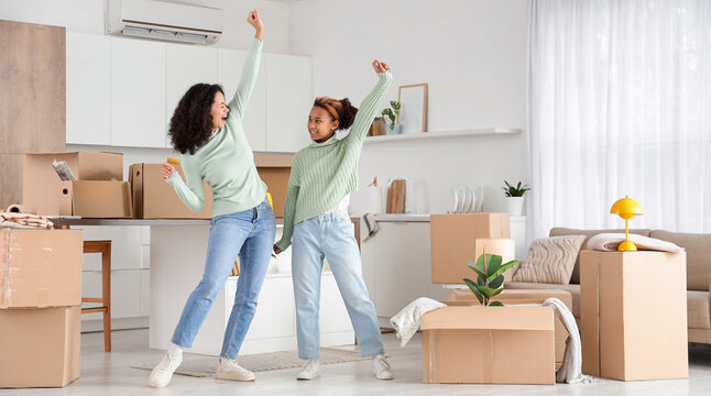 New home excitement and moving day, happy mother and daughter dancing with cardboard boxes in a modern apartment living room and kitchen area