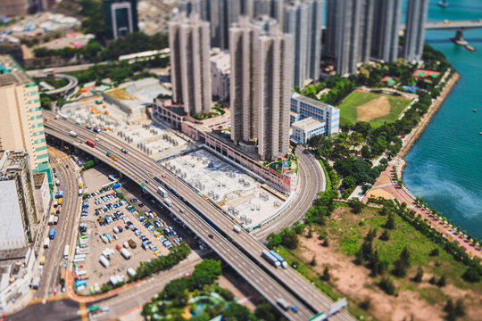 Miniature tilt-shift perspective of a busy highway and parking area beside urban high-rises