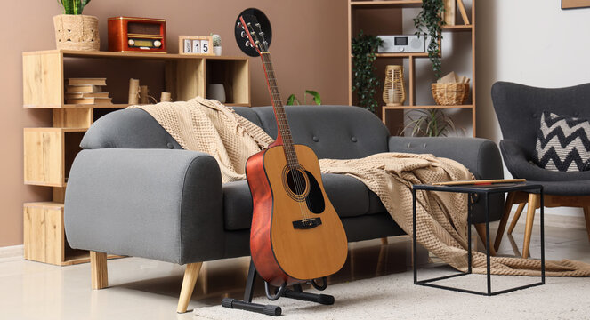 Music hobby and creative lifestyle, acoustic guitar on a stand in a cozy modern living room interior with a grey sofa and home decor