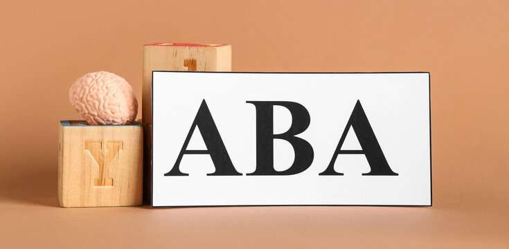 Applied behavior analysis and autism therapy, brain health and cognitive development with wooden blocks and model on a brown background