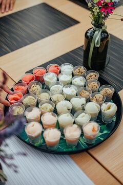 Tray filled with small cups of assorted ice cream samples in multiple flavors and colors, presented on a table with decorative flowers for a tasting event