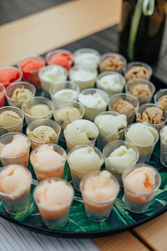 Tray filled with small cups of assorted ice cream samples in multiple flavors and colors, presented on a table with decorative flowers for a tasting event