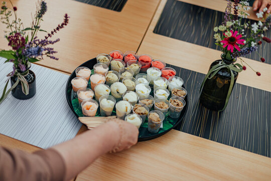 Tray filled with small cups of assorted ice cream samples in multiple flavors and colors, presented on a table with decorative flowers for a tasting event