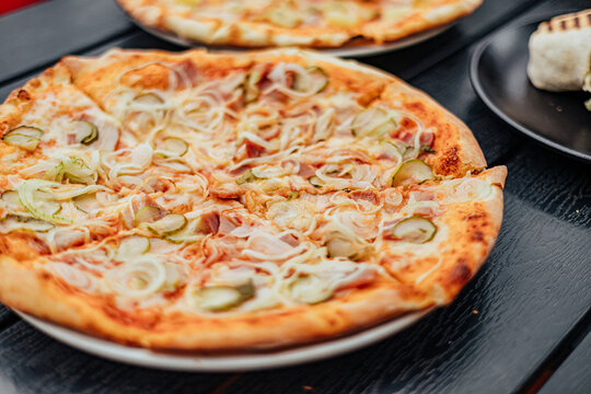 Close-up of freshly baked pizza topped with cheese, onion, pickles and ham, with a second pizza softly blurred in the background
