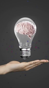 Animation of human brain in light bulb on cropped hand of caucasian woman against black background
