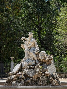 Sculptural detail of the Genius of Palermo fountain in the sunny grounds of Villa Giulia, framed by dense green foliage and traditional stone inscriptions.