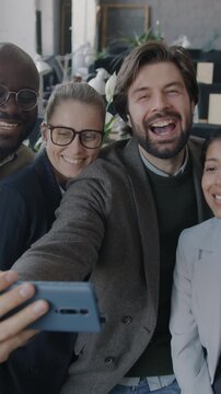 Multiethnic group of businesspeople having fun in office taking selfie with smartphone camera laughing grimacing. Business and photo concept.