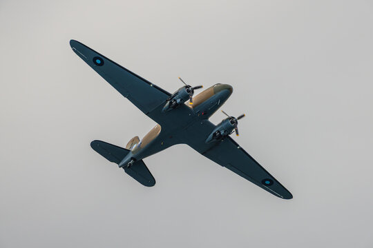 A classic twin-engine military transport plane flies through a clear, overcast sky during an aerial demonstration