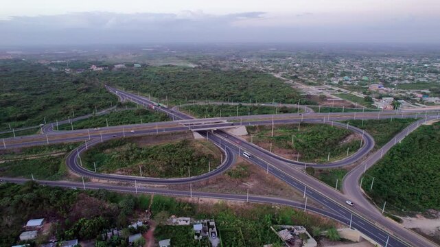High-angle aerial drone shot ascending and flying forward over a cloverleaf highway interchange at dusk, capturing vehicle traffic driving along overpass bridges and loops