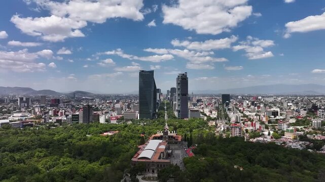 A breathtaking cinematic aerial drone view looking down from the historic Chapultepec Castle across the lush green canopy of Bosque de Chapultepec toward the soaring skyscrapers.