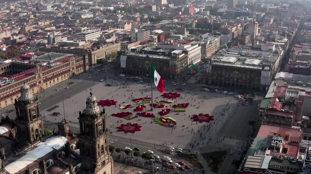 A breathtaking cinematic aerial view capturing the historic Z&oacute;calo square, the colossal Mexican flag, and the prominent bell towers of the Metropolitan Cathedral in the historic center of Mexico City.
