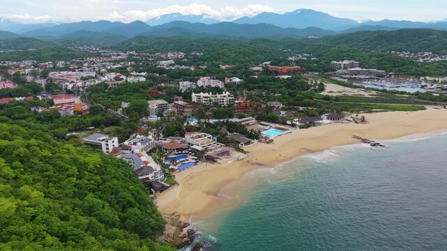 A breathtaking cinematic aerial drone view capturing the scenic golden-sand expanse of Playa Chahu&eacute;, its clear blue-green waters, and coastal palm fringe in Bah&iacute;as de Huatulco, Oaxaca, Mexico.