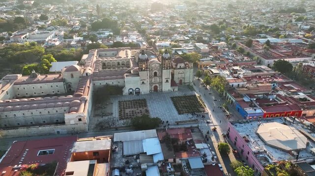 A breathtaking cinematic aerial drone view capturing the historic Templo de Santo Domingo de Guzm&aacute;n and its adjacent former monastery, surrounded by the colorful colonial street grid of Oaxaca City.