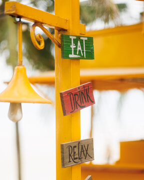 Wooden Eat Drink Relax Signs on Yellow Post with Bell Close-Up