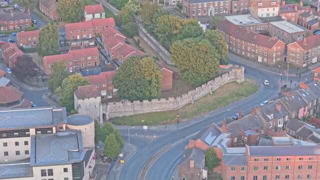 York Castle curtain wall borders Tower Street in York, England, with historic brick buildings and curved urban roads surrounding the medieval defensive complex, drone push-in.
