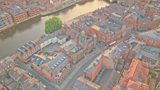 York Magistrates' Court stands on Clifford Street beside the River Ouse, with ornate red brickwork, clock tower and domed towers in the historic centre, aerial establishing shot.